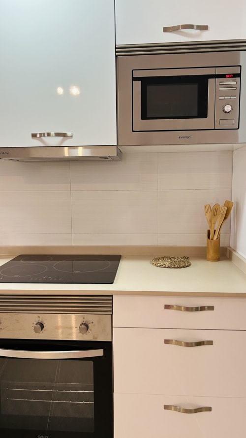 Modern kitchen in Baeza apartment with stainless steel appliances, induction cooktop, built-in microwave, and wooden utensils