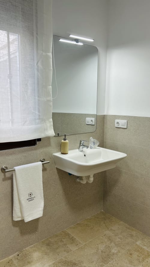 Modern bathroom with white sink, illuminated mirror, and beige tile walls at Alojamientos Estrella Baeza in Baeza