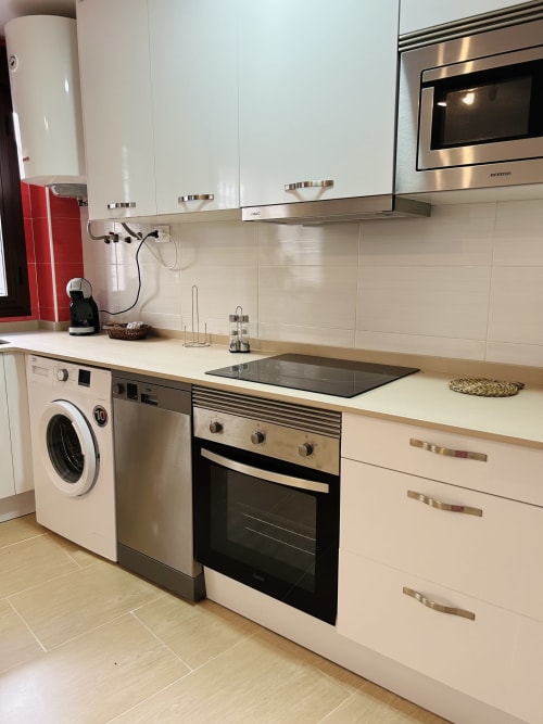 Modern kitchen in Baeza apartment with white cabinets, stainless steel appliances, and washing machine