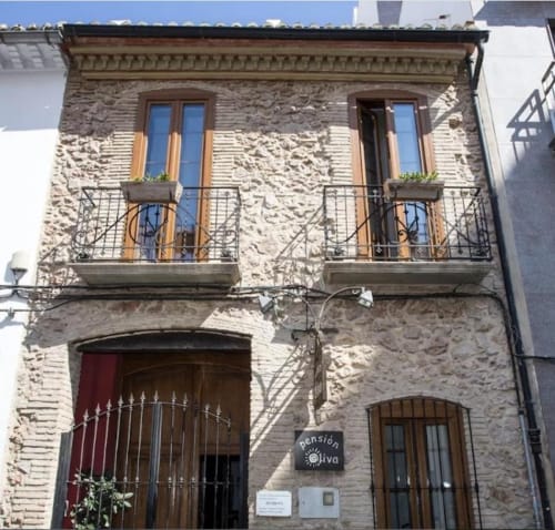 Hotelito Oliva Pensión exterior en Oliva, España. Edificio histórico de piedra con dos balcones, puertas de madera y barandillas de hierro.