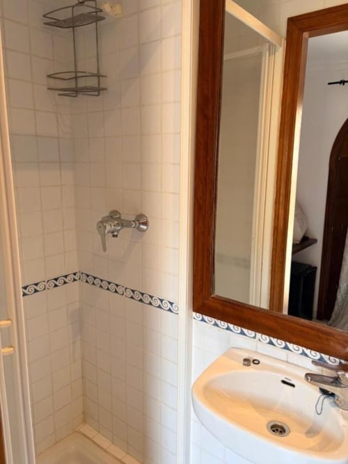 Baño moderno en Hotelito Oliva Pensión de Oliva con ducha de azulejos blancos, lavamanos y espejo con marco de madera