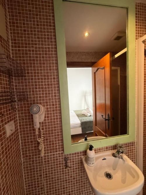 Baño del Hotelito Oliva con lavamanos, espejo, paredes de azulejos rojos y ducha a 2km de la playa en Oliva