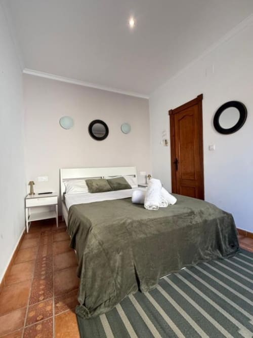 Amplio dormitorio doble en Hotelito Oliva Pensión en Oliva con suelos de terracota, ropa de cama en tonos oliva y comodidades modernas.