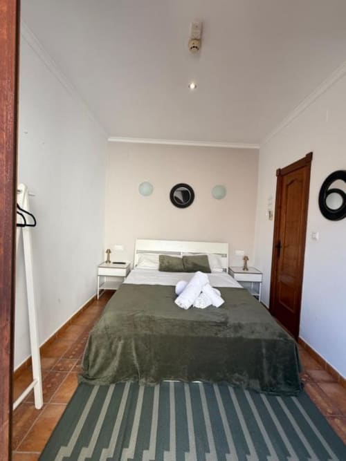 Moderno dormitorio doble en Hotelito Oliva Pensión en Oliva con ropa de cama verde oliva, almohadas blancas y piso de madera