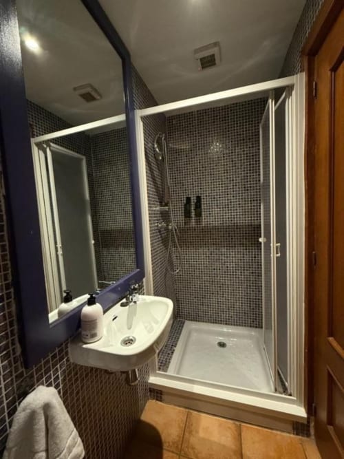 Baño moderno con paredes de mosaico oscuro, lavamanos blanco y ducha con mamparas de cristal en Hotelito Oliva Pensión