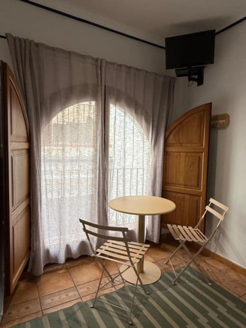 Habitación doble en Hotelito Oliva Pensión con mesa redonda, sillas, ventanas arqueadas con cortinas y puertas de madera en Oliva
