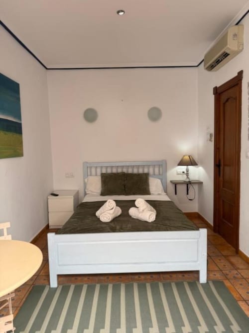 Moderno dormitorio doble en Hotelito Oliva Pensión en Oliva, España, con cama blanca, ropa de cama oscura, toallas enrolladas y aire acondicionado