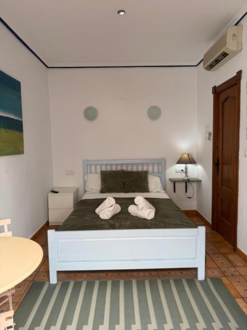 Moderno dormitorio doble en Hotelito Oliva Pensión en Oliva con cama blanca, ropa de cama oscura, puerta de madera, aire acondicionado y