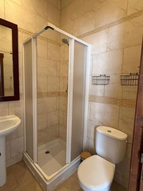 Baño moderno con cabina de ducha blanca, inodoro y paredes con azulejos beige en Hotelito Oliva Pensión, Oliva