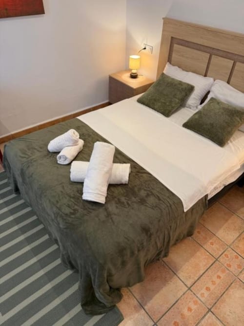 Habitación doble en Hotelito Oliva Pensión con dos camas, almohadas verdes, toallas enrolladas y lámpara de mesilla