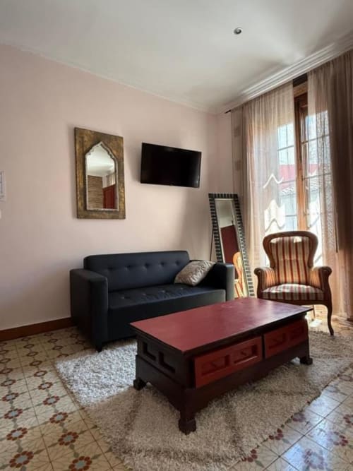 Elegante habitación en Hotelito Oliva con sofá negro, mesa roja, sillón rayado, TV en pared y vistas a la ciudad cerca de Oliva
