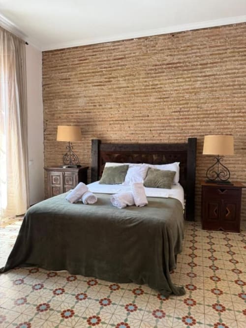 Elegante habitación doble en Hotelito Oliva con pared de ladrillo, cama de madera oscura, ropa de cama verde, mesitas con lámparas y detalles estampados