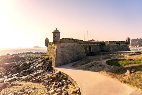 Fortaleza histórica costeira em Maia, Portugal com praia arenosa e costa rochosa ao pôr do sol