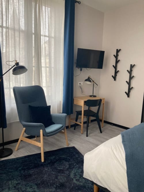Chambre moderne du Relais de Touraine avec fauteuil bleu, bureau, télévision et lumière naturelle des fenêtres