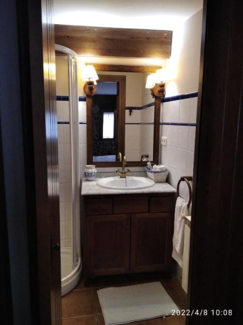 Baño moderno con vanidad de madera oscura, lavabo redondo, espejo con apliques, detalles de azulejos azules y puerta de ducha curva en Casa