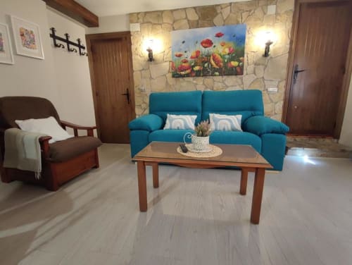 Acogedora sala de estar en Casa Lahuerta en Bronchales con sofá turquesa, mesita de madera y muro de piedra
