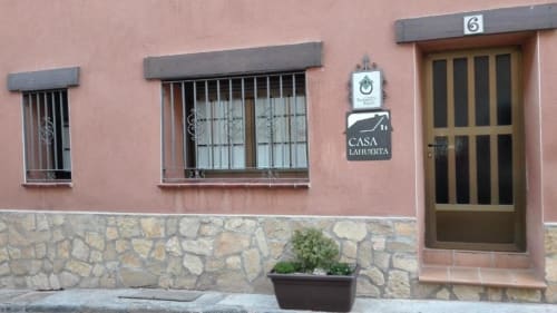 Exterior del apartamento rural Casa Lahuerta en Bronchales con fachada de terracota, puerta de madera, ventanas enrejadas y base de piedra