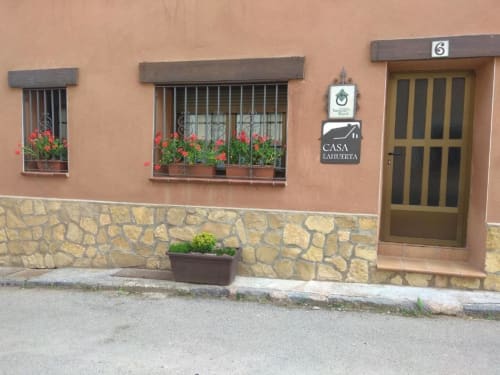 Entrada del estudio rural Casa Lahuerta en Bronchales con fachada de terracota, ventanas con rejas y flores rojas, base de piedra