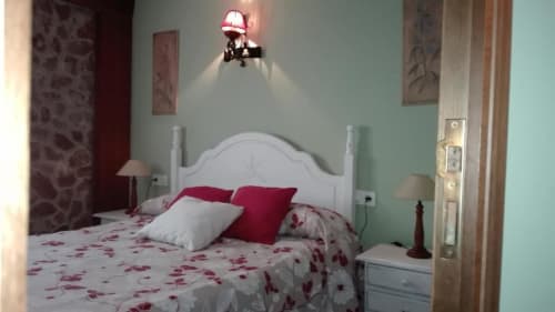 Dormitorio luminoso en Casa Lahuerta con cabecero blanco, ropa de cama floral roja, paredes menta y lámparas de mesita gemelas en Bronchales