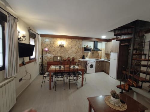 Cocina abierta y comedor en apartamento Casa Lahuerta, Bronchales con mesa de madera, armarios oscuros, electrodomésticos blancos