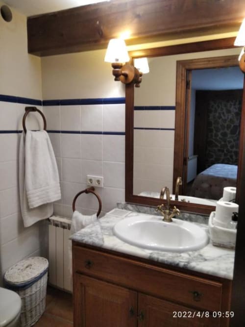 Baño de Casa Lahuerta en Bronchales con lavabo de mármol, tocador de madera, azulejos blancos, espejo y herrajes de latón