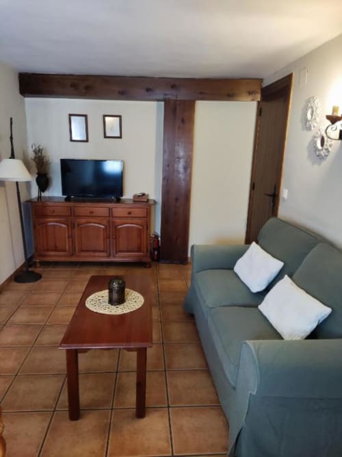 Sala de estar del estudio Casa Lahuerta con sofá verde, muebles de madera, TV y suelo de baldosas terra cotta en Bronchales