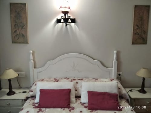 Dormitorio con cama de cabecera blanca, almohadas burdeos, ropa de cama floral, lámpara de pared y mesillas en Casa Lahuerta