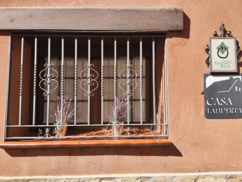 Exterior del alojamiento rural Casa Lahuerta con rejas de hierro decorativas y señal de Turismo Rural en Bronchales, España