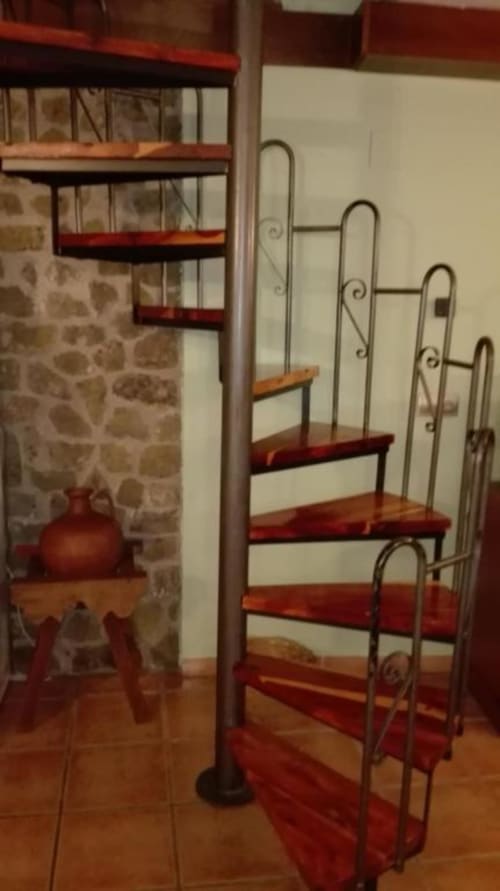 Escalera de caracol con peldaños de madera roja y barandillas de hierro forjado en el apartamento Casa Lahuerta, Bronchales