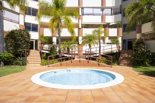 Circular pool surrounded by terracotta tiles, palm trees, and modern apartment building at RB Algarve hotel in Vilamoura,