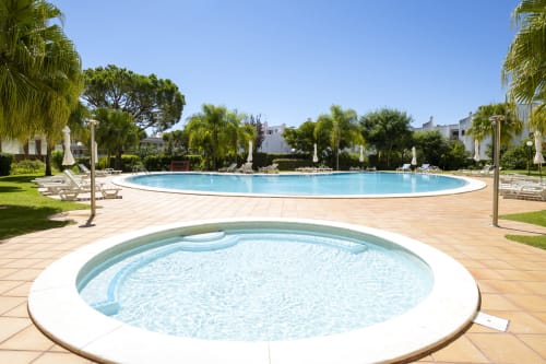 Circular hot tub and large oval pool at RB Algarve resort in Vilamoura, with palm trees and white apartment buildings