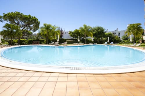 Large circular swimming pool at RB Algarve hotel in Vilamoura, Portugal, surrounded by palm trees and loungers