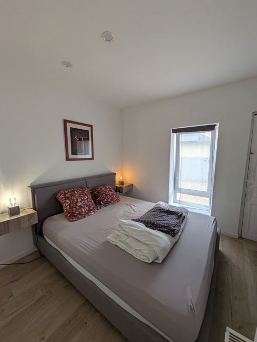 Chambre moderne à la Résidence des dunes à Landéda avec lit gris, oreillers rouges, porte vitrée et éclairage chaleureux