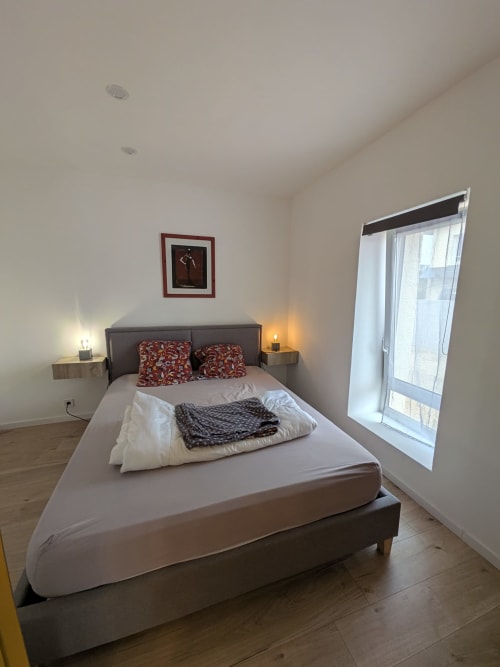 Chambre moderne à la Résidence des dunes à Landéda avec lit gris, coussins rouges, lampes de chevet et baie vitrée coulissante vers