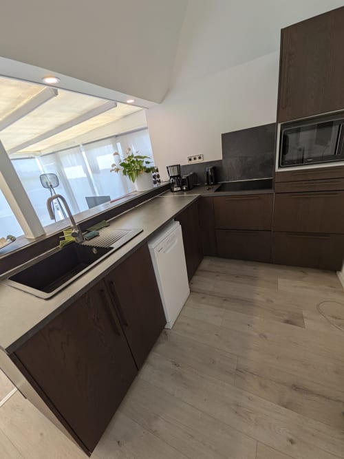Cuisine moderne de la Résidence des dunes avec meubles en bois foncé, plan de travail noir, évier et électroménagers