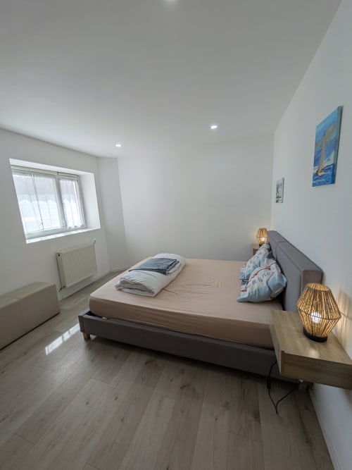 Chambre moderne à la Résidence des dunes à Landéda : lit gris, parquet, baie vitrée et décoration murale côtière