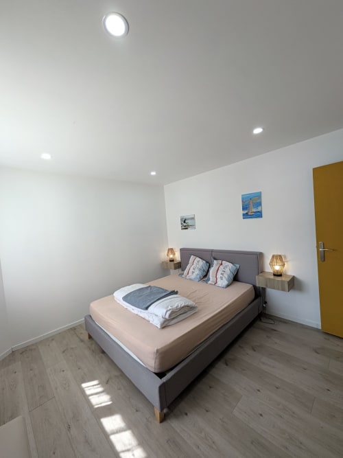 Chambre moderne de la Résidence des dunes à Landéda avec lit gris, parquet, murs blancs et porte jaune