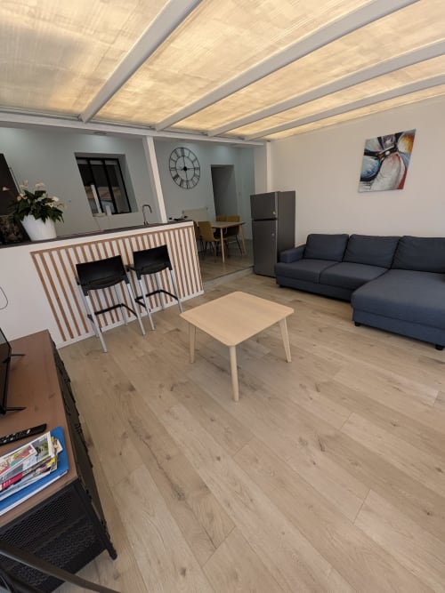 Espace de vie ouvert et moderne à la Résidence des dunes avec canapé sombre, kitchenette, table à manger et plafond éclairé.