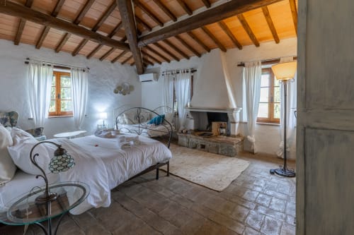 Spacious bedroom suite in Tuscan hotel with wooden beamed ceiling, fireplace, wrought iron bed, and countryside views