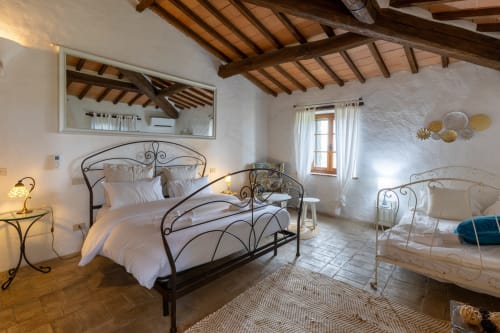 Spacious bedroom at Quarantallina hotel in Buonconvento, Italy, featuring wrought iron beds and wooden beam ceiling
