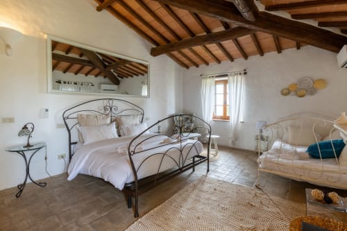 Rustic bedroom in Buonconvento hotel with wrought iron beds, wooden beams, and terracotta floors