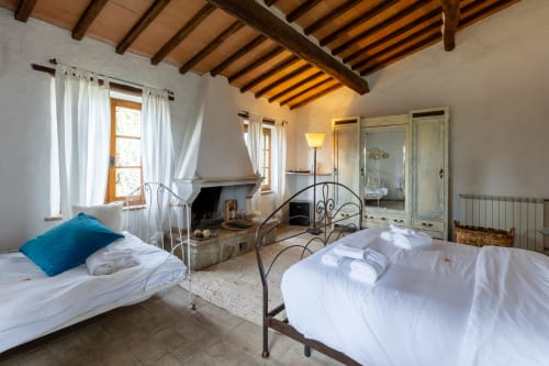 Spacious bedroom with two beds, fireplace, and wooden beams at Quarantallina hotel in Buonconvento, Italy