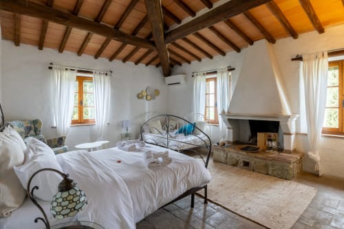 Spacious bedroom with fireplace at Quarantallina hotel in Buonconvento, featuring wooden beams, white linens, and windows