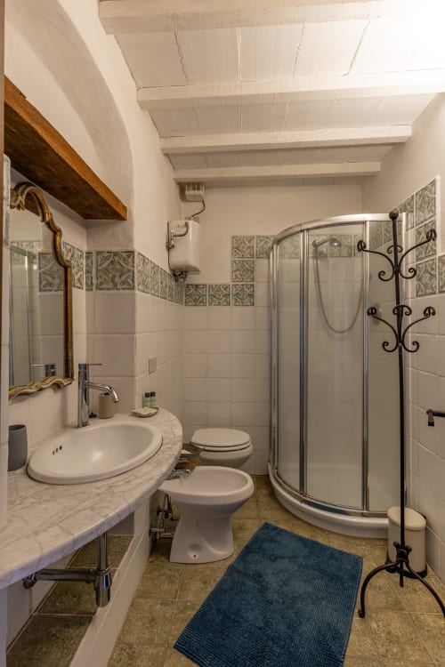 Modern bathroom with marble vanity, curved shower enclosure, decorative tilework, and wooden ceiling beams in Buonconvento