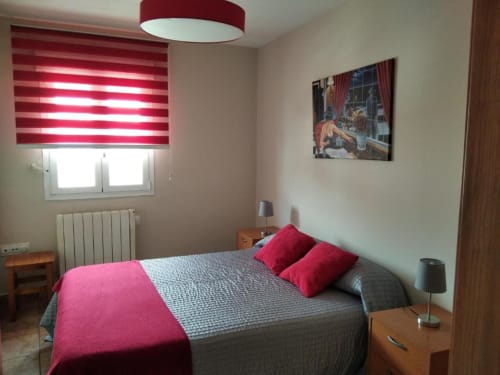 Dormitorio en Casa Rural El Abuelo Lahuerta en Bronchales con detalles rojos, cama doble y ventana con vistas a la ciudad