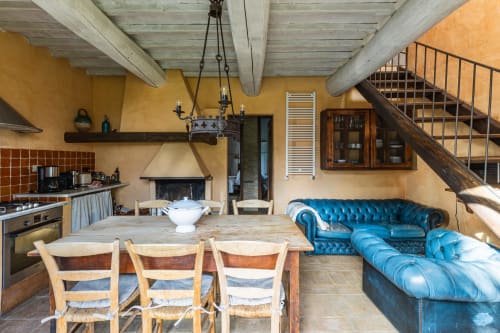 Appartamento rustico toscano con divano chesterfield blu, travi in legno, pareti gialle, zona pranzo e cucina aperta