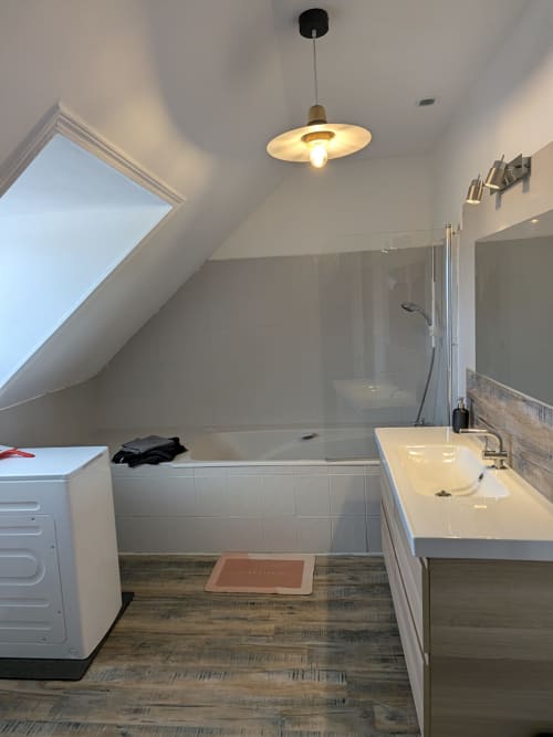 Salle de bain moderne sous les combles de la Résidence des dunes avec carrelage blanc, lavabo, baignoire et puits de lumière à Landéda