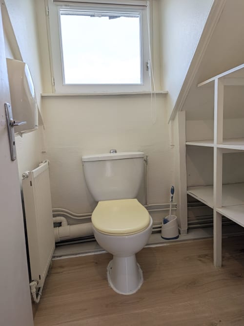Salle de bains avec toilettes, siège jaune, radiateur et fenêtre de toit à la Résidence des dunes de Landéda
