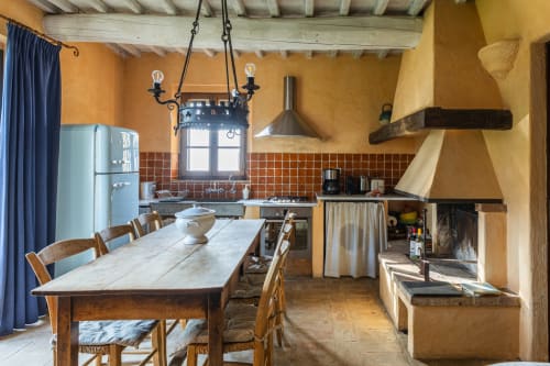 Cucina e zona pranzo rustica a Buonconvento con pareti gialle, tavolo in legno e camino tradizionale