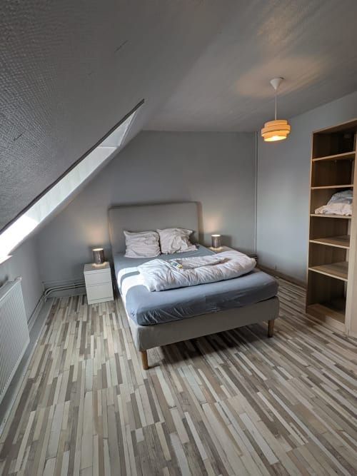 Chambre loft moderne à la Résidence des dunes à Landéda avec lit capitonné gris, étagères en bois et plafond mansardé